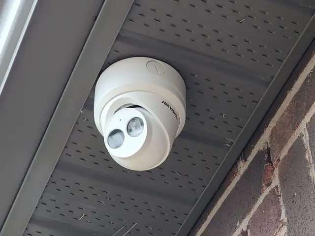 White turret camera under a grey soffit beside a brick wall
